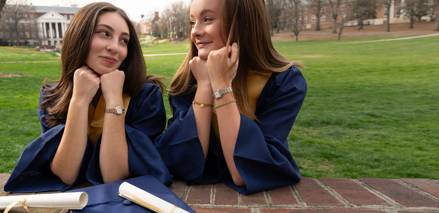 Graduation Gift Guide; Image of two women in their graduation caps and gowns wearing Sutton and Surveyor watch models 96R256 and 98L331